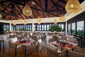Ein geräumiges Restaurant mit hohen Decken, großen Fenstern und Korbmöbeln.