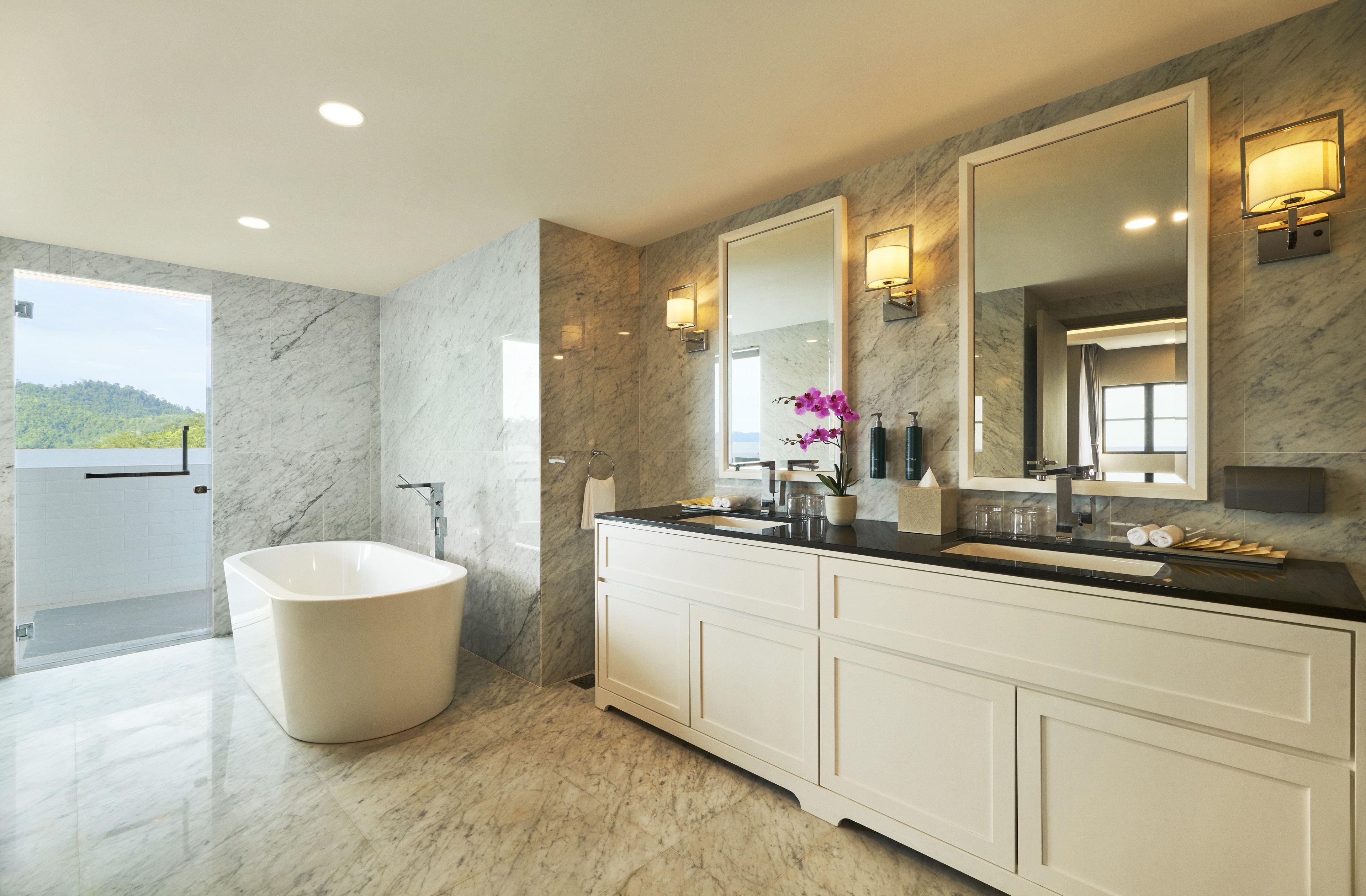 A modern bathroom with a freestanding bathtub, a large vanity with a mirror, and a view of a natural landscape.