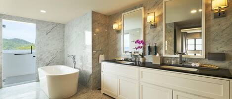 A modern bathroom with a freestanding bathtub, a large vanity with a mirror, and a view of a natural landscape.