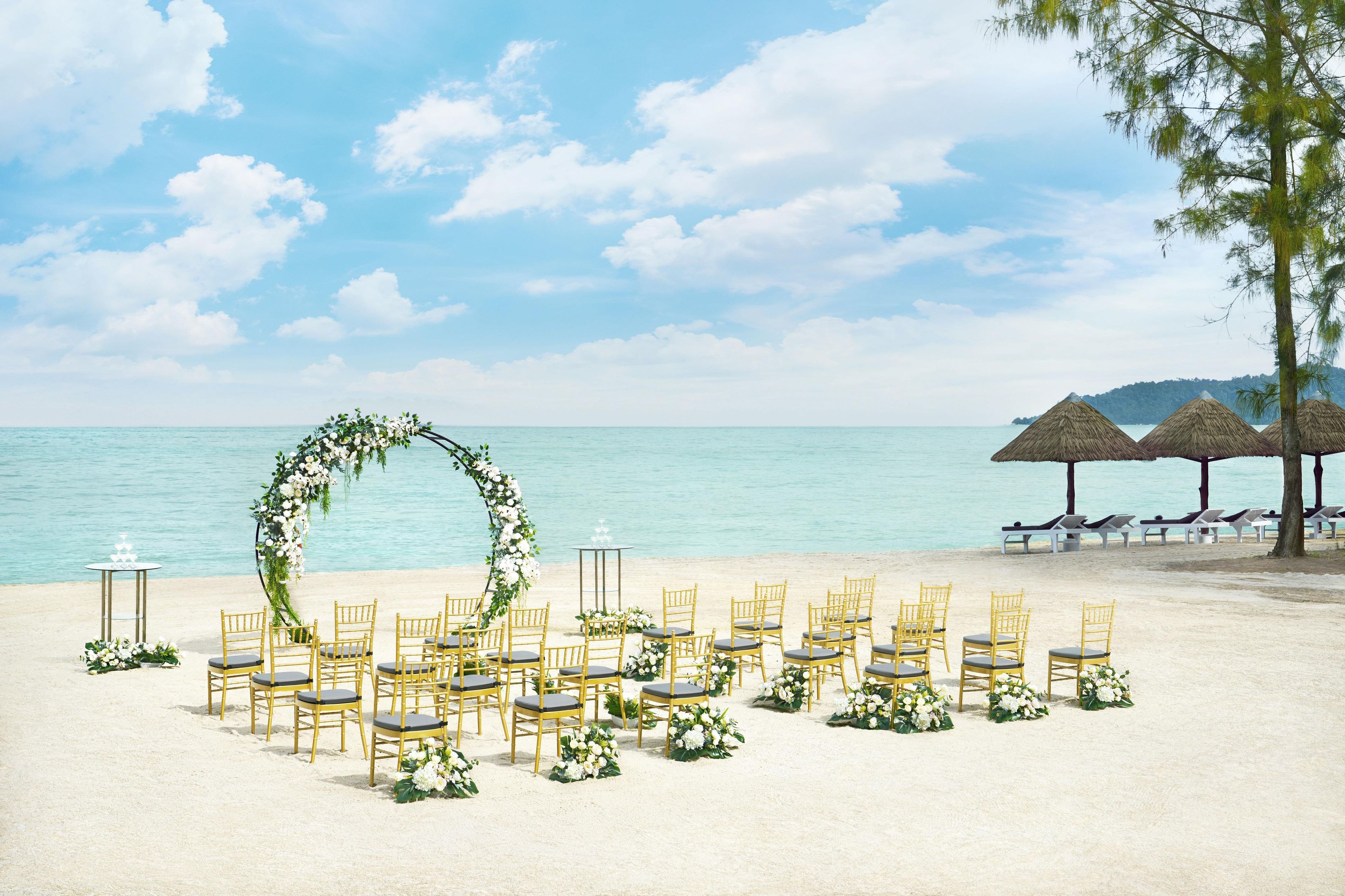 Montaje para una boda en la playa, con sillas y un arco floral.