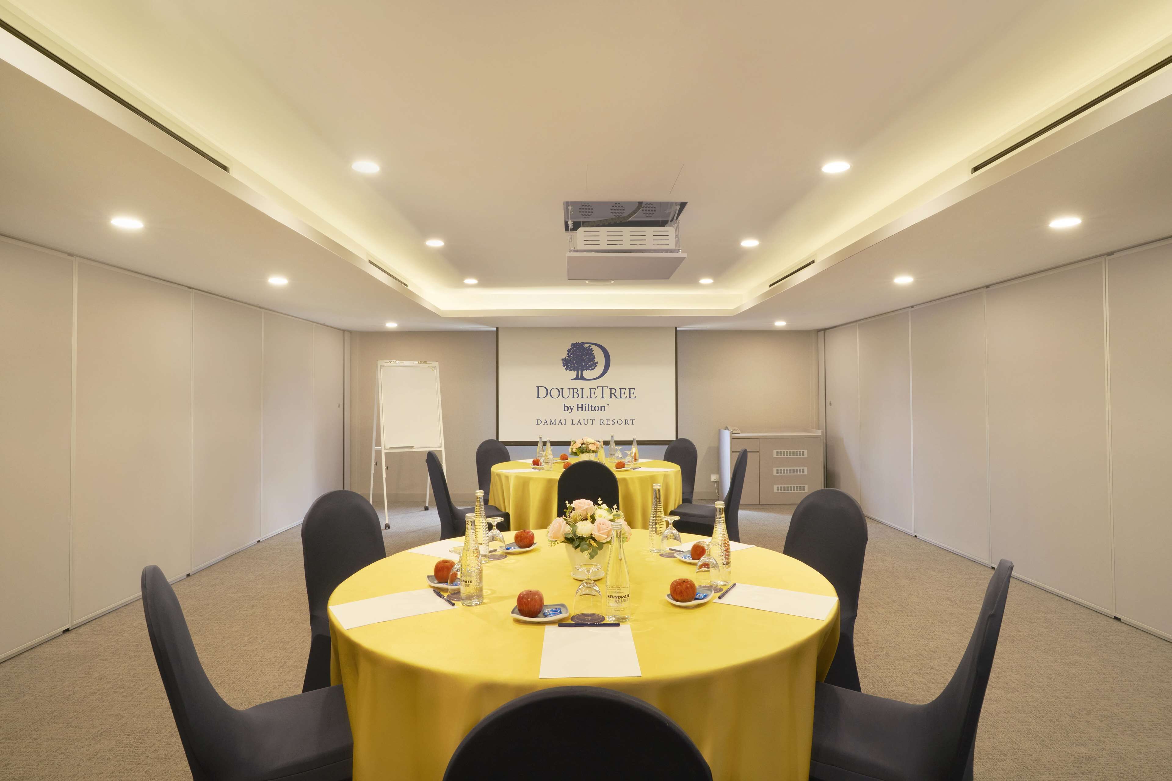 A conference room with a yellow table, black chairs, and a sign reading "DoubleTree by Hilton DAMAI LAUT RESORT".
