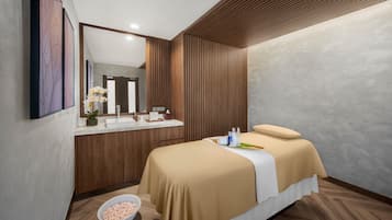 A modern bathroom with a wooden vanity, a large mirror, and a bed with a beige bedspread.