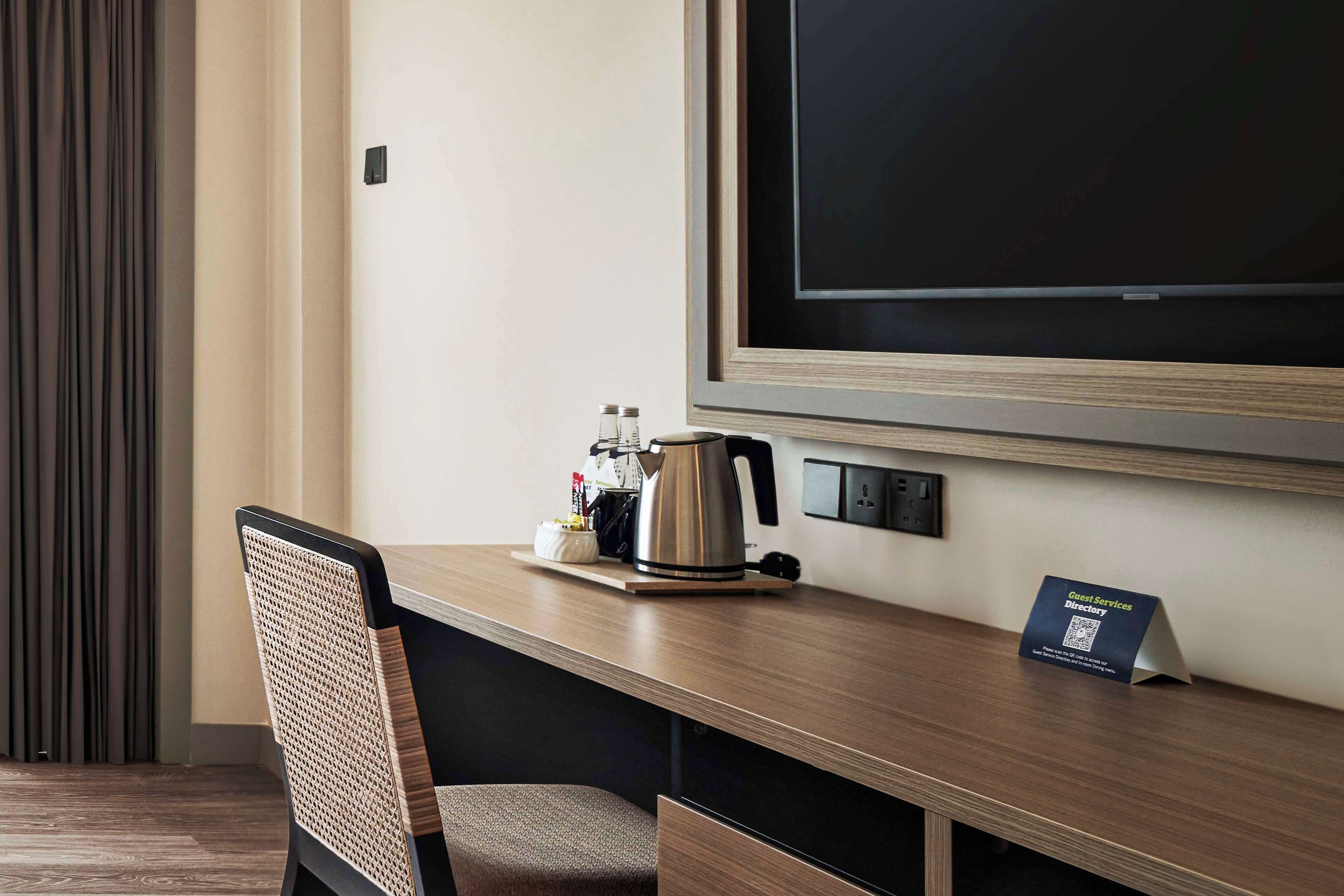 A hotel room with a wooden desk, a chair, a coffee maker, and a signboard.