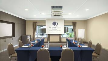 Une salle de conférence équipée d’une longue table, de chaises, d’un écran de projection et d’une banderole sur laquelle on peut lire : « DOUBLETREE by Hilton DAMAT LAUT RESORT ».