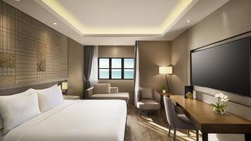 A hotel room with a bed, a desk, a chair, a television, and a window with a view of the sea.