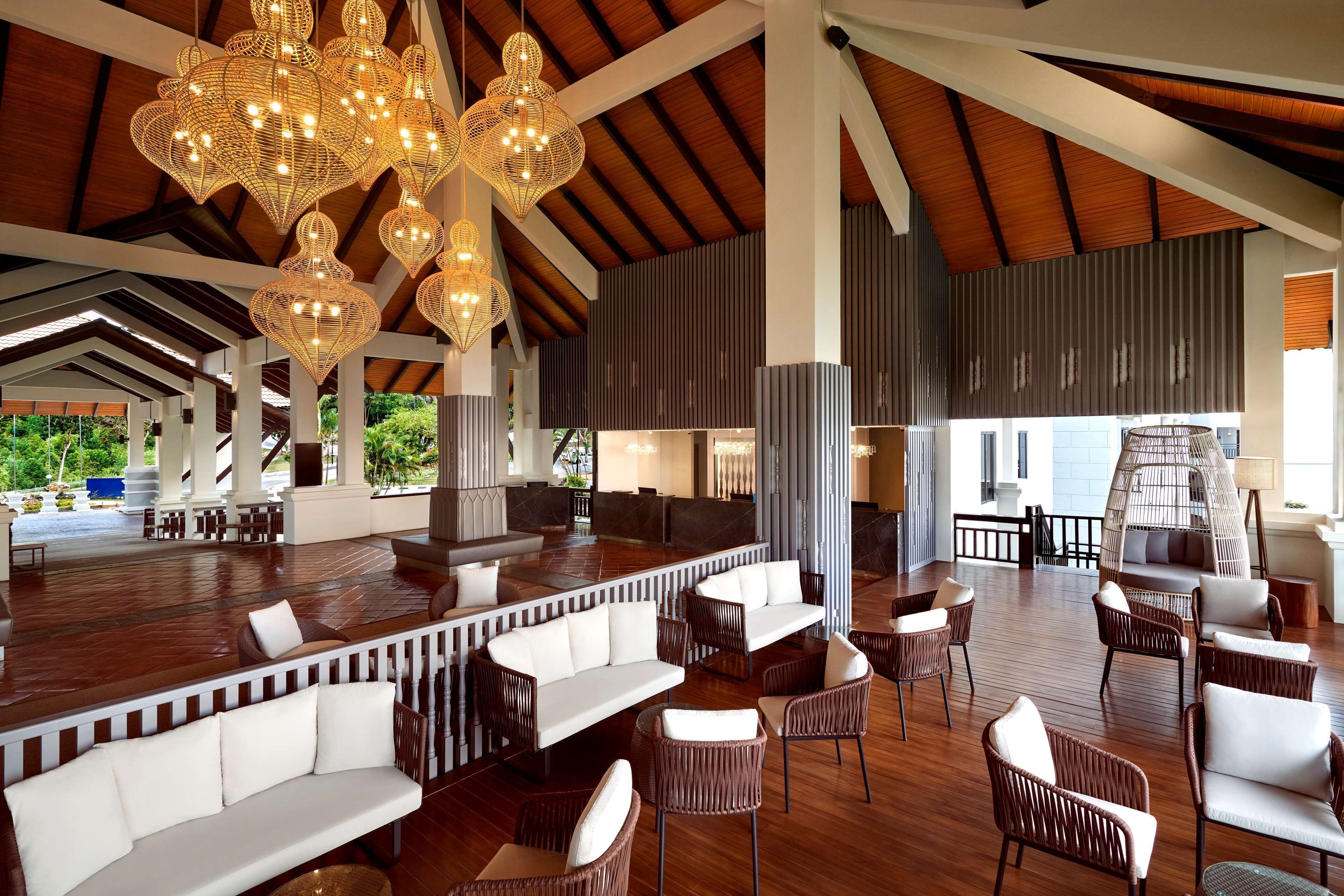 A spacious outdoor lounge area with wooden flooring, white cushioned seating, and decorative wicker chandeliers.