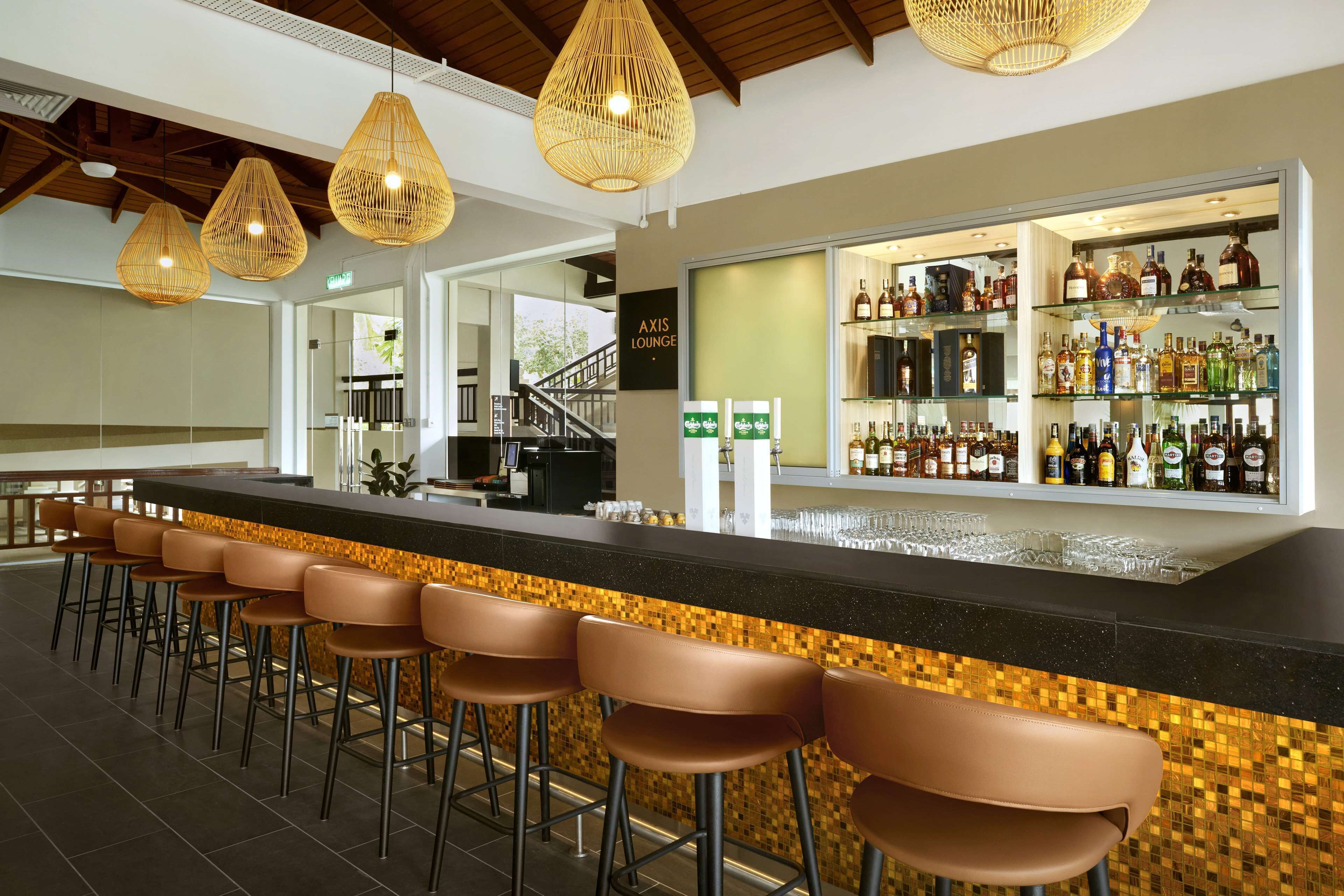 A bar area with a long counter, multiple stools, and a variety of bottles and glasses on shelves.