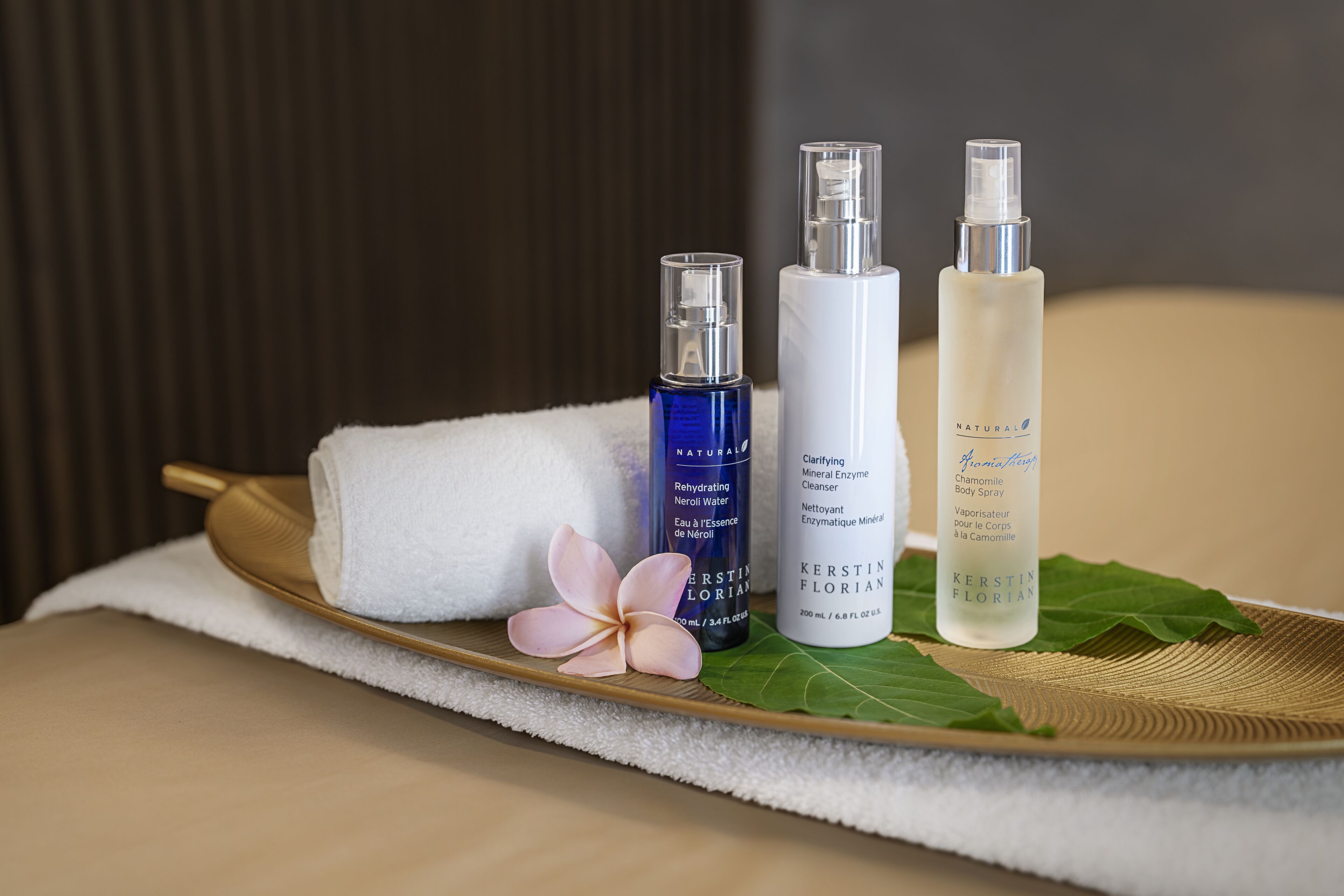 Three bottles of body spray on a tray with a towel and a flower.