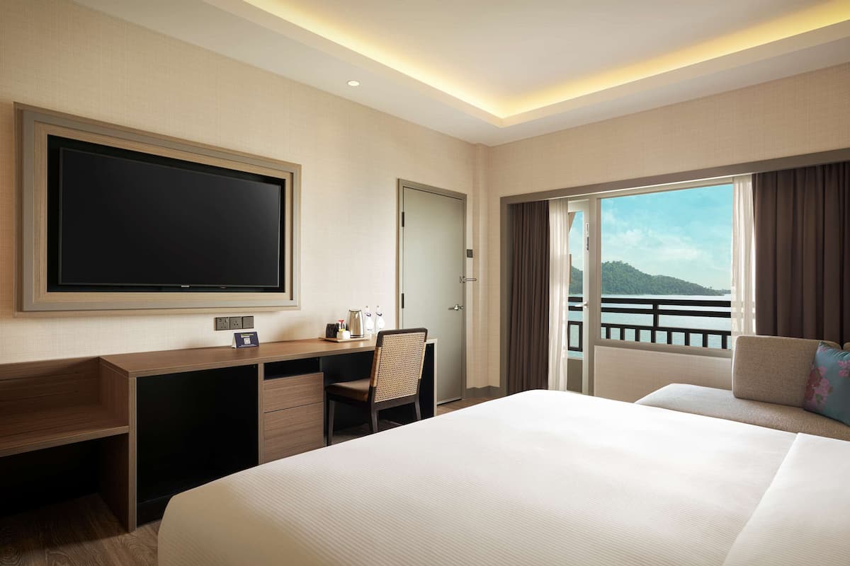 Ein Hotelzimmer mit einem großen Bett, einem Schreibtisch mit Stuhl, einem Flachbildfernseher und einem Balkon mit Meerblick.