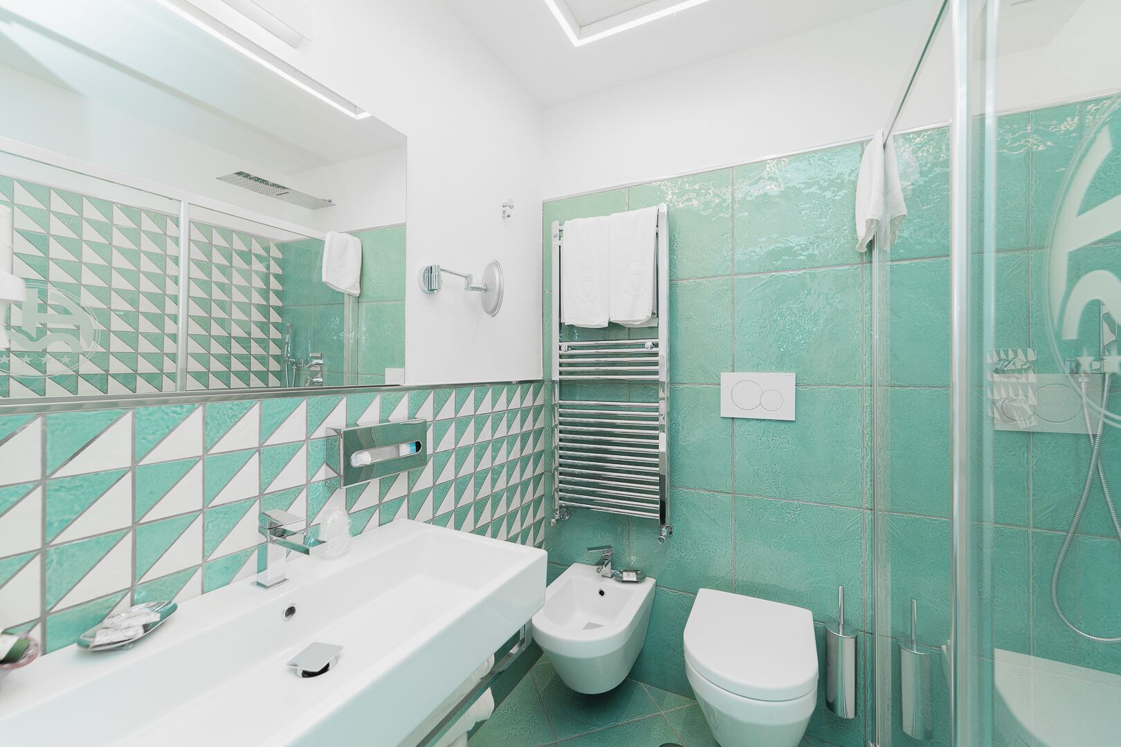 Un baño moderno con lavamanos, bidé e inodoro blancos, y una cabina de ducha de vidrio.