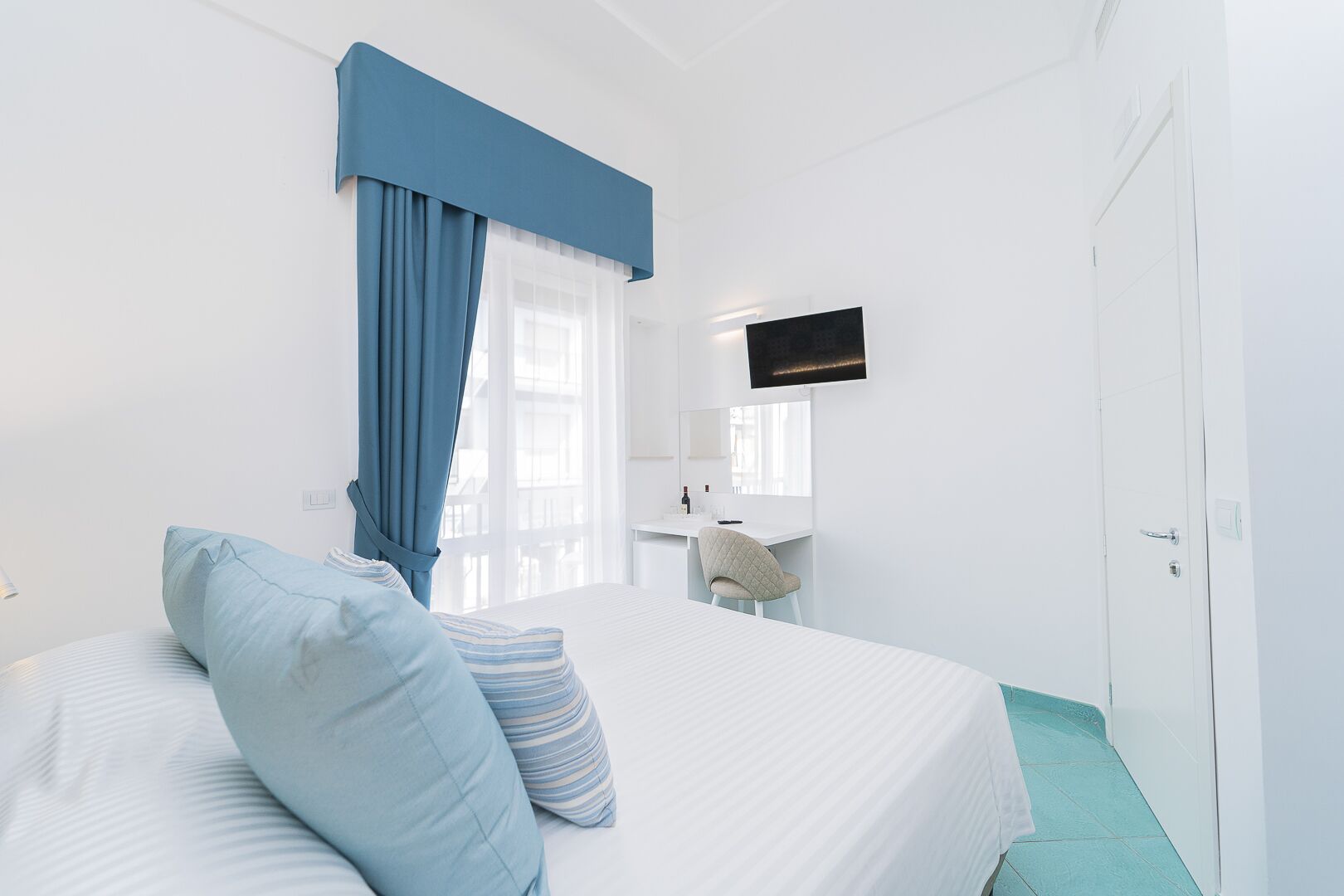 A hotel room with a bed, a desk, a chair, a television, and a wardrobe.