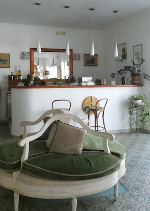 Ein Zimmer mit einer runden, gepolsterten Sitzecke, einer Holztresen mit diversen Gegenständen und hängenden Pendelleuchten.