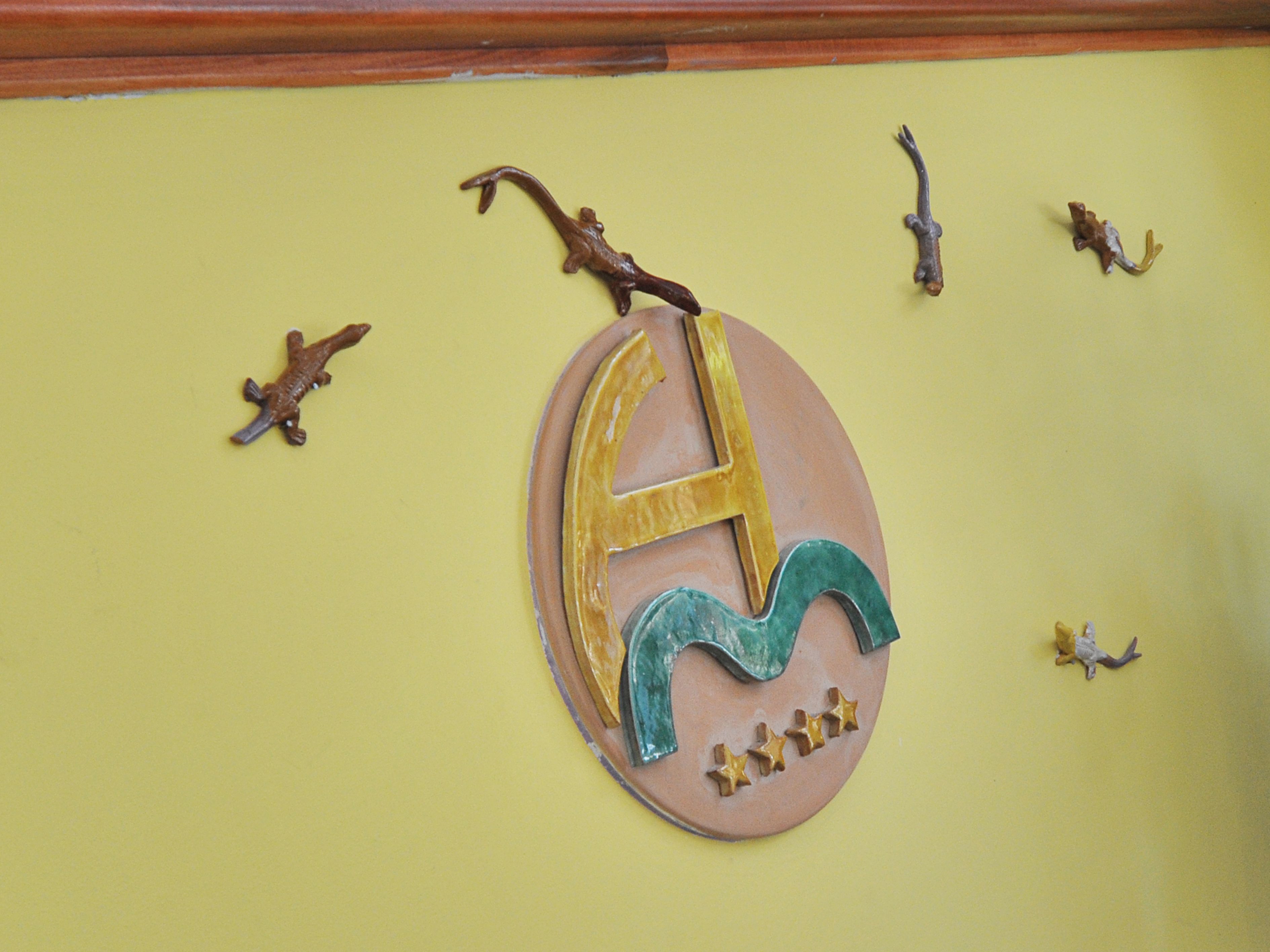 Una pared con un emblema decorativo que muestra una letra 'H' estilizada y un diseño de ola, rodeado de pequeñas figuras de animales.