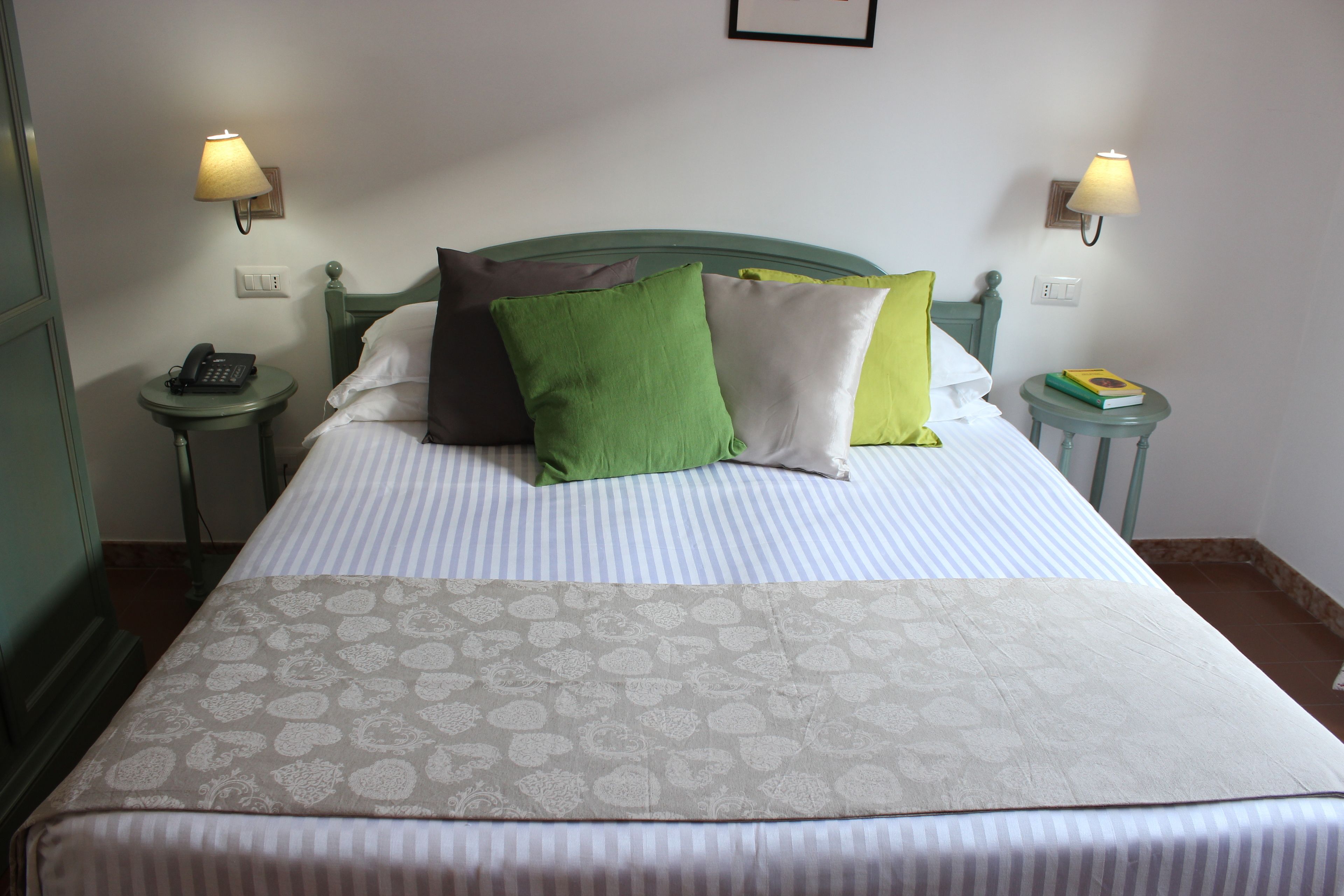 Cama bem arrumada com roupa de cama listrada e almofadas decorativas, duas luminárias de cabeceira e um telefone de mesa.