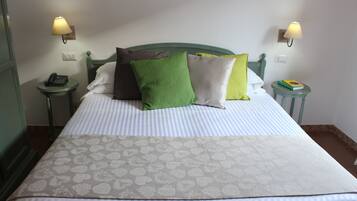 Cama bem arrumada com roupa de cama listrada e almofadas decorativas, duas luminárias de cabeceira e um telefone de mesa.