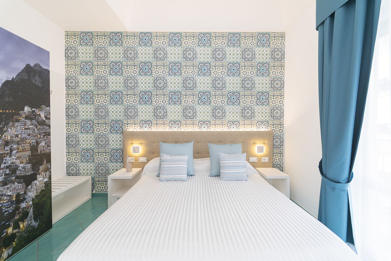 Un dormitorio con pared decorada, cama con ropa de cama a rayas y vistas a un paisaje urbano.