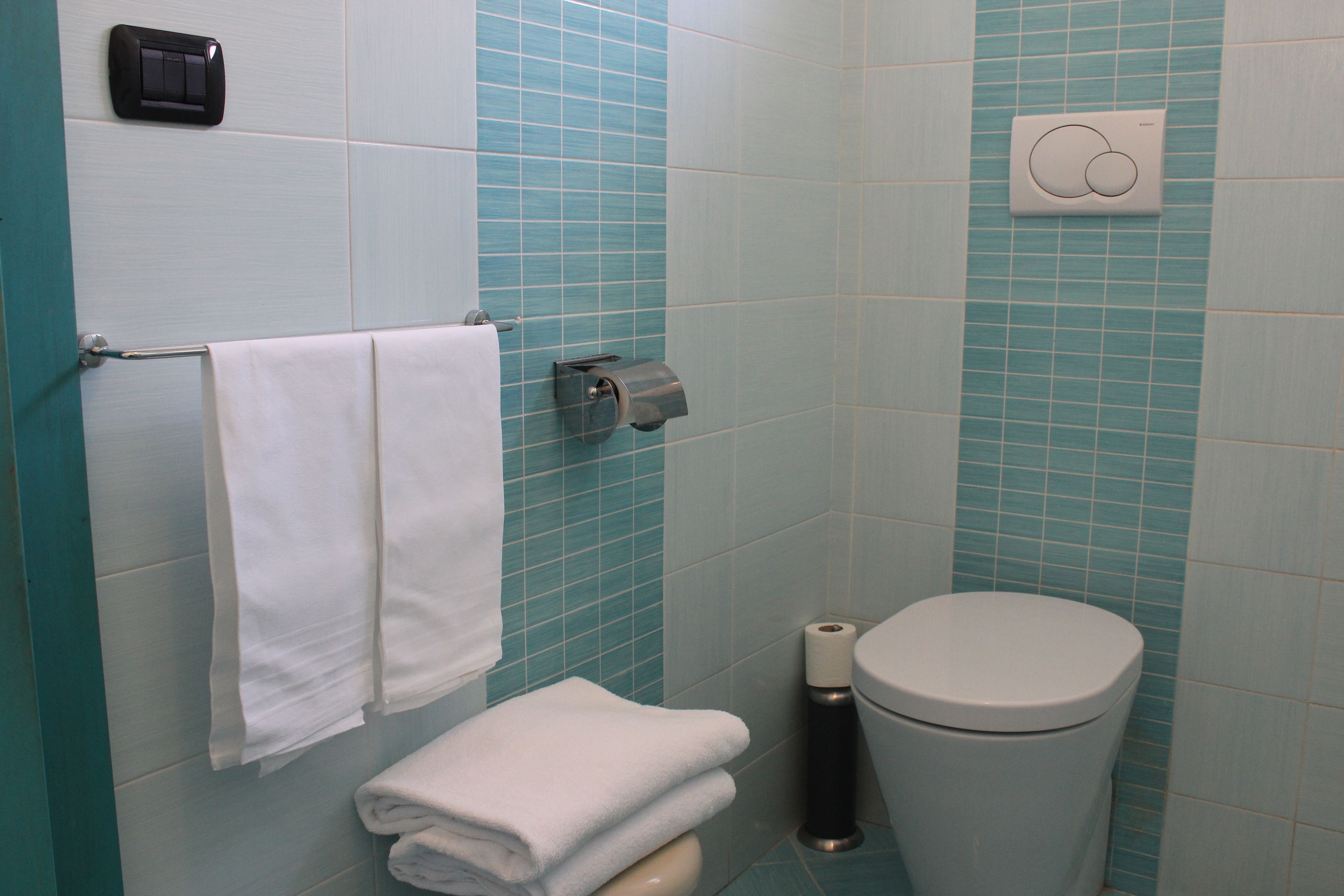 Un baño con inodoro, toallero con toallas dobladas, dispensador de servilletas de papel y dispensador de jabón en la pared.