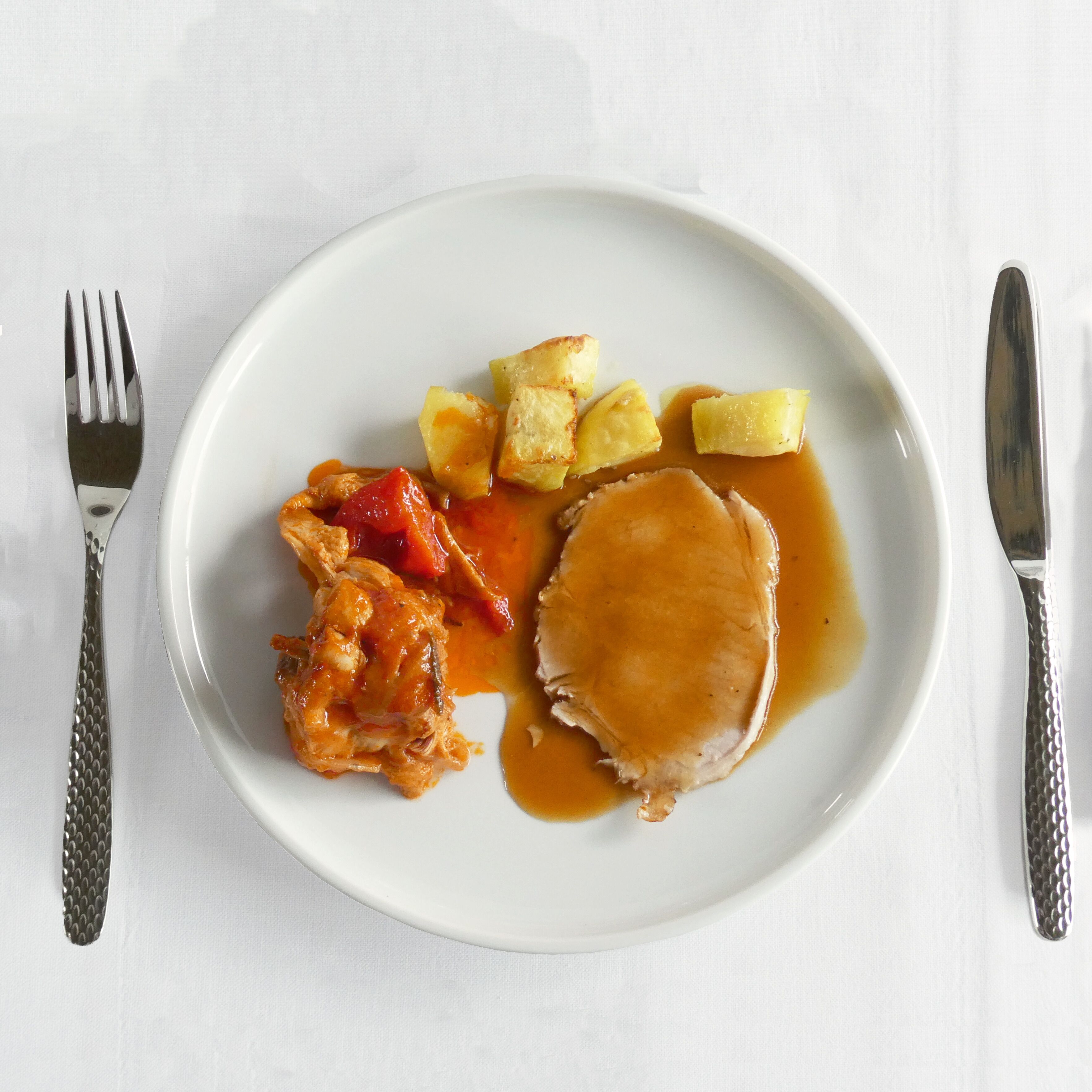 A white plate with a piece of meat, diced potatoes, and a sauce.