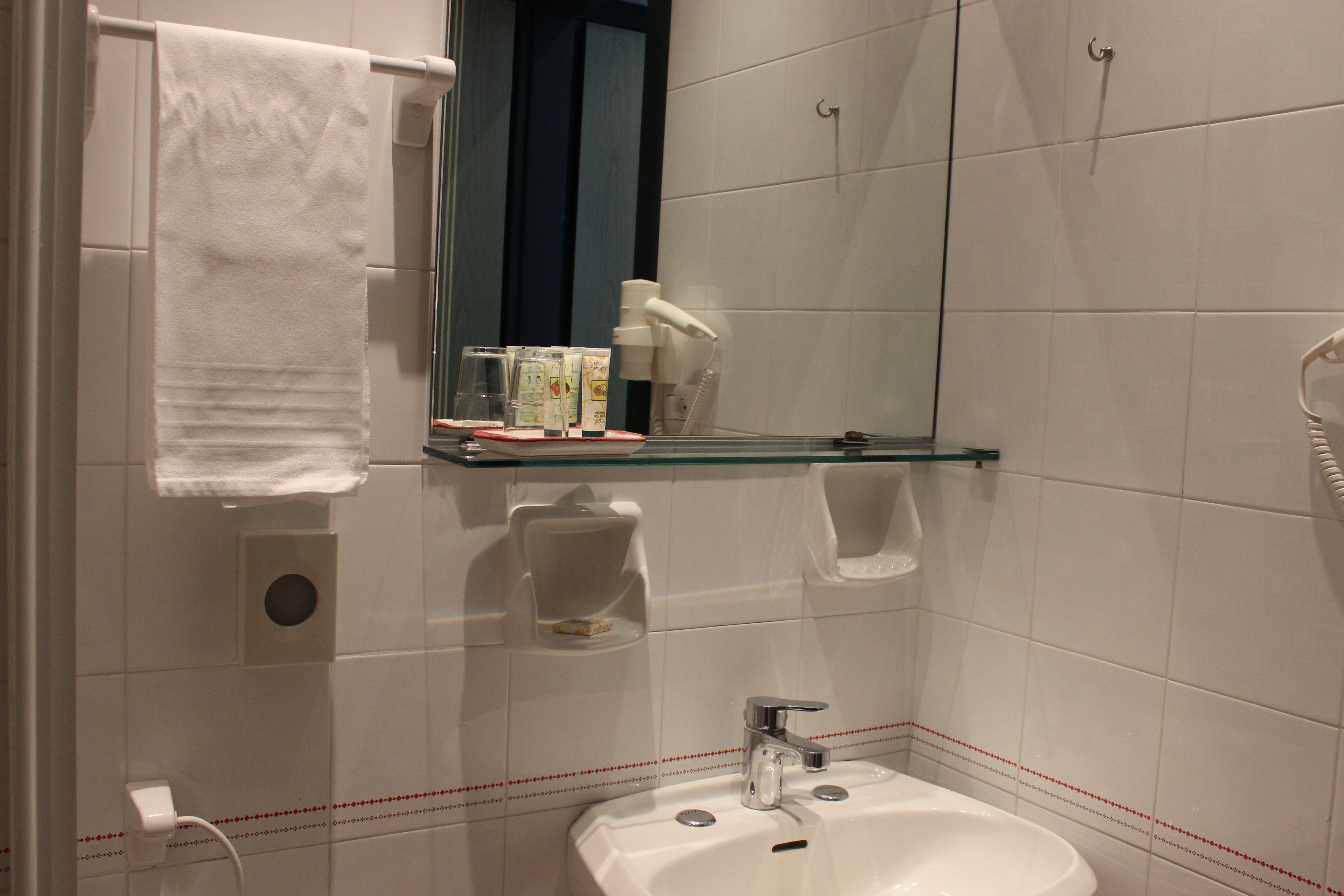 A bathroom with a white sink, a mirror, a towel hanging on a rack, and a glass shelf with toiletries.