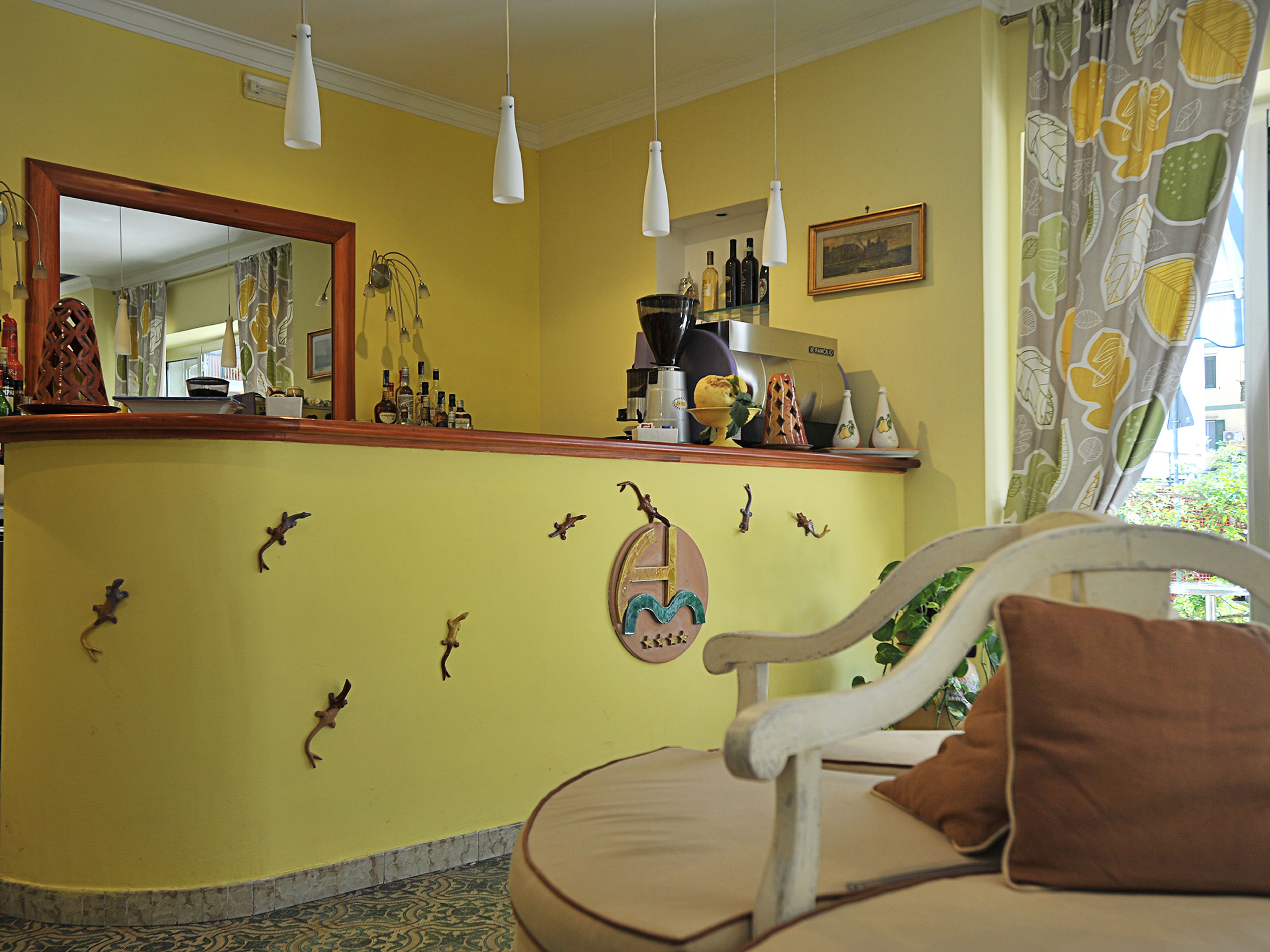A room with a yellow wall, a wooden bar counter, a mirror, and a white chair with a brown pillow.