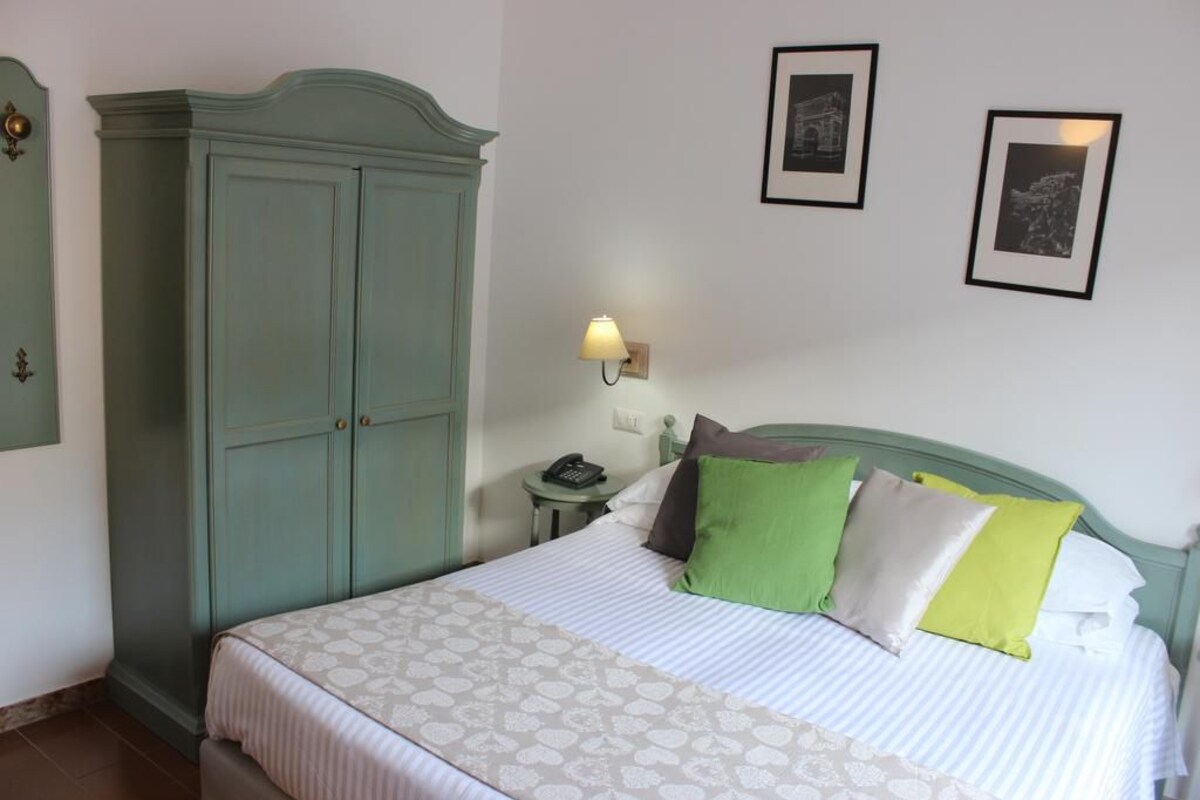 A neatly made bed with patterned bedding, a green headboard, and a bedside lamp.