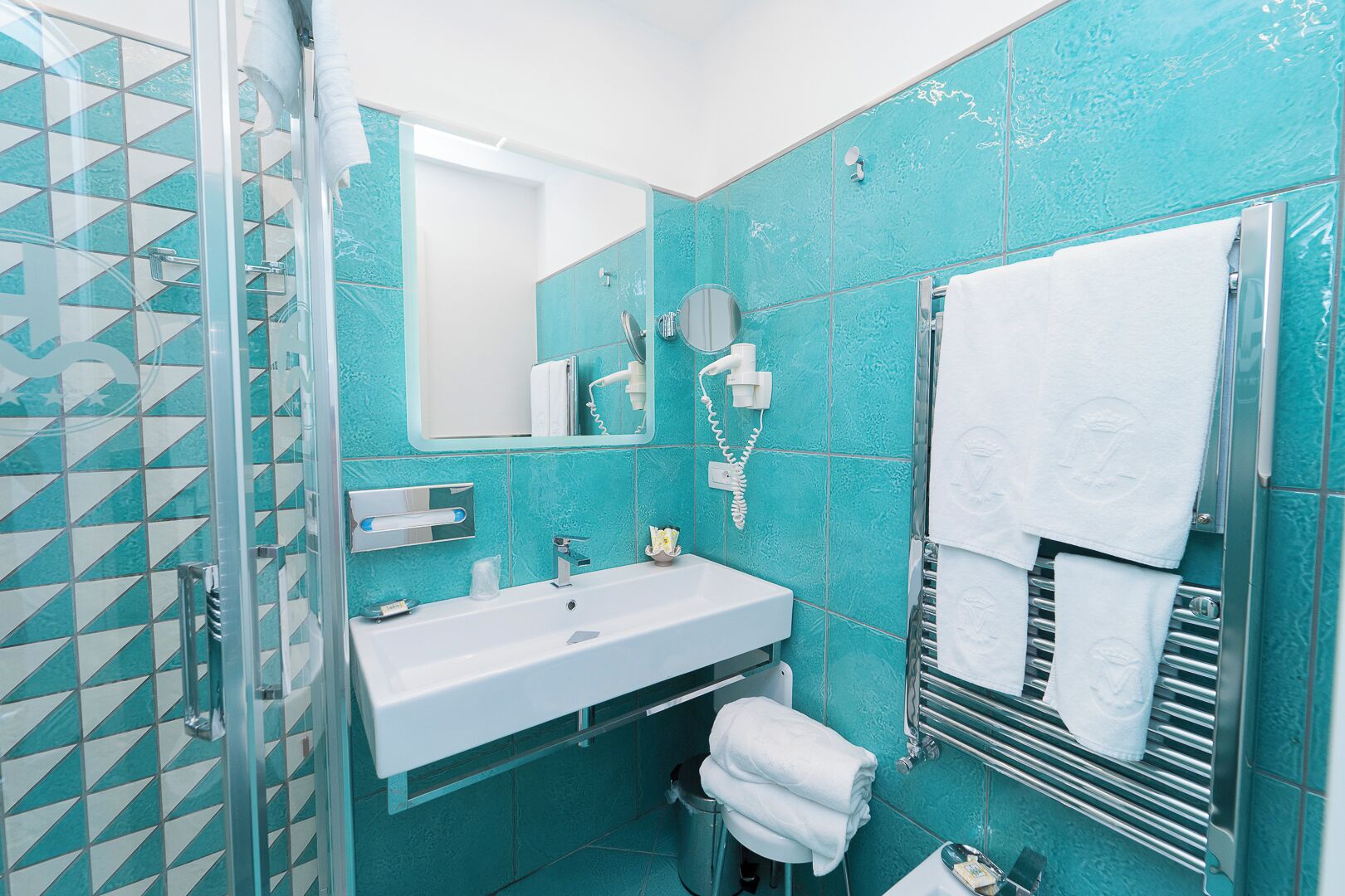 Un bagno con cabina doccia in vetro, lavandino, specchio e porta asciugamani.