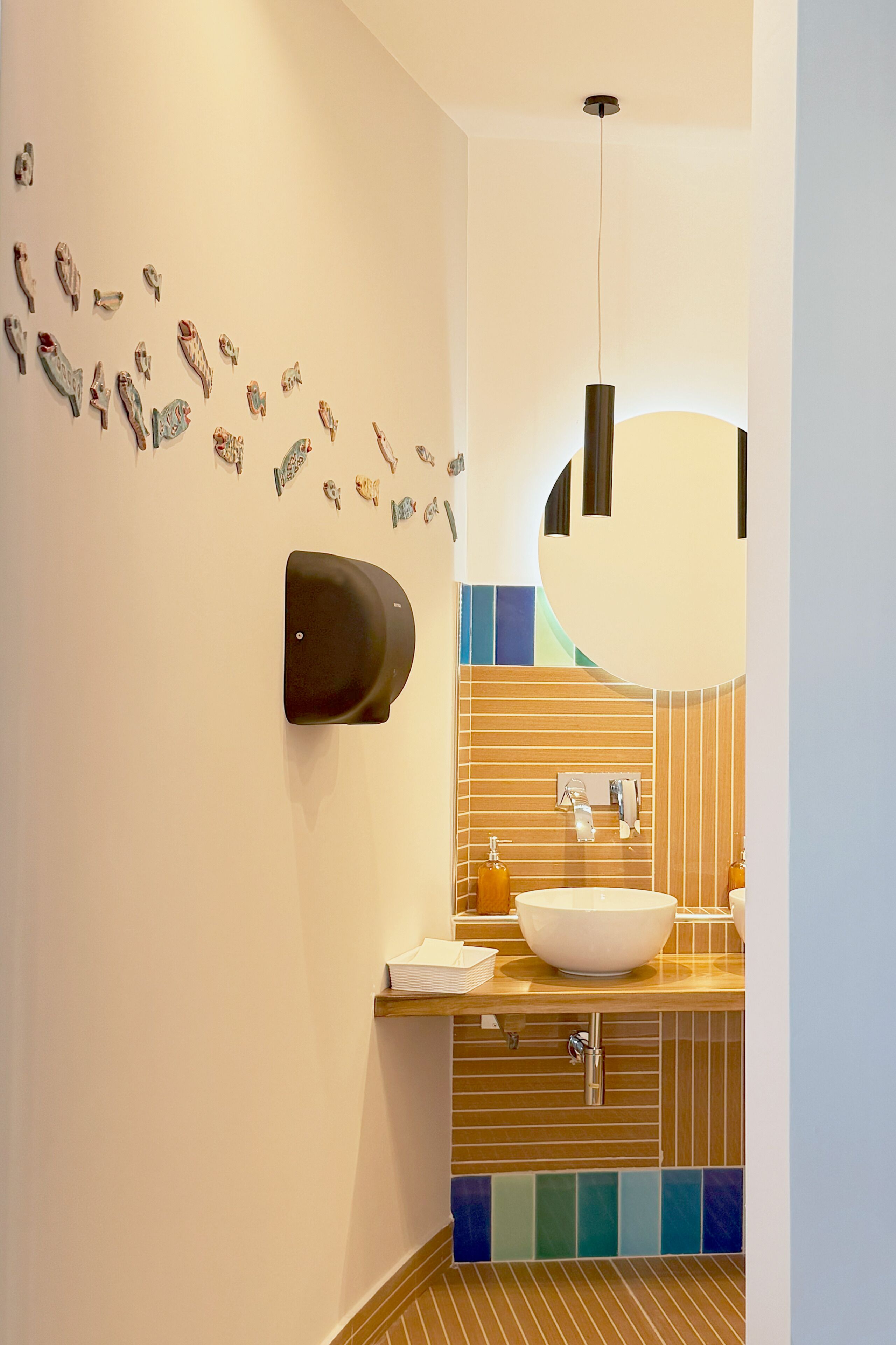 Un baño moderno con un lavamanos montado en la pared, un espejo grande y detalles decorativos en la pared.
