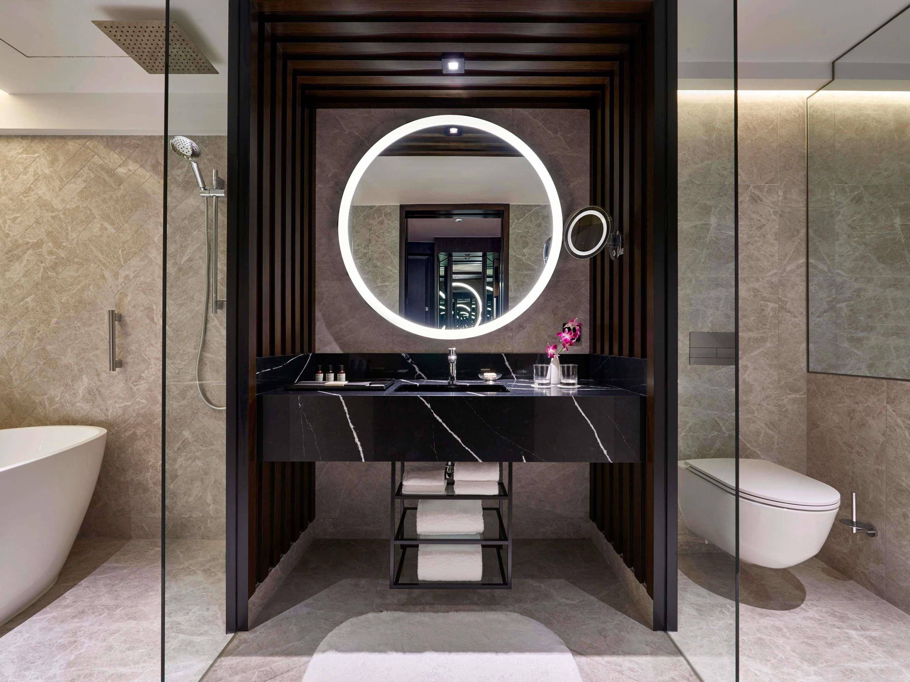 A modern bathroom with a black marble vanity, a large mirror, a showerhead, and a toilet.