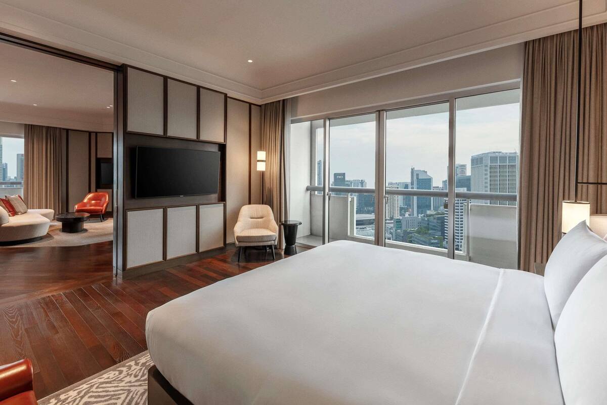 Una habitación de hotel moderna con una cama grande, un sofá, una silla, un televisor y vistas a la ciudad.