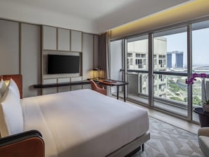 A hotel room with a bed, a TV, a desk, and a large window with a city view.
