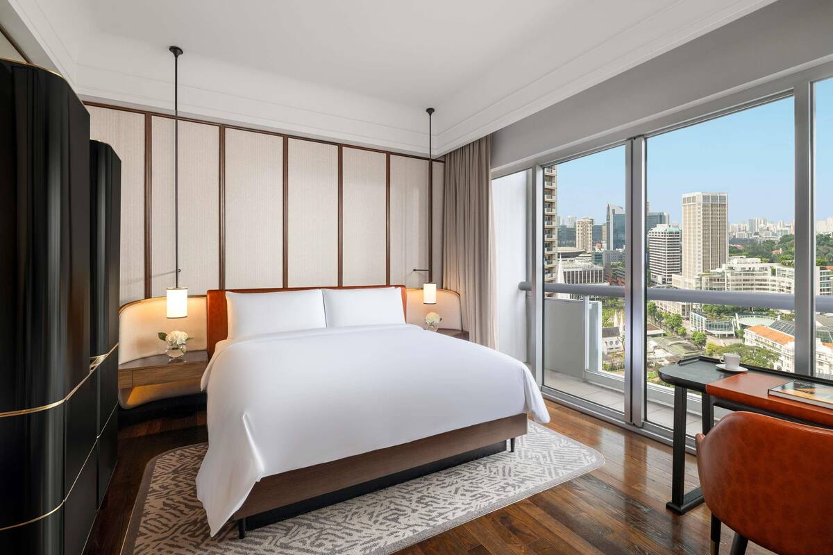 A modern hotel room with a large bed, a desk, and a view of the city.