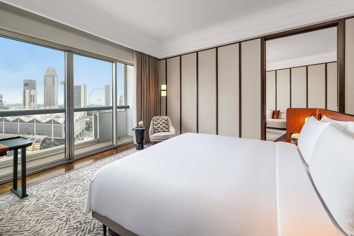 A hotel room with a large bed, a chair, a small table, and a view of the city skyline.