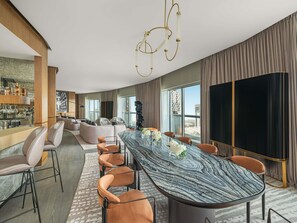 Een moderne hotelkamer met een marmeren eettafel, lederen stoelen, een bar en grote ramen met uitzicht op de stad.