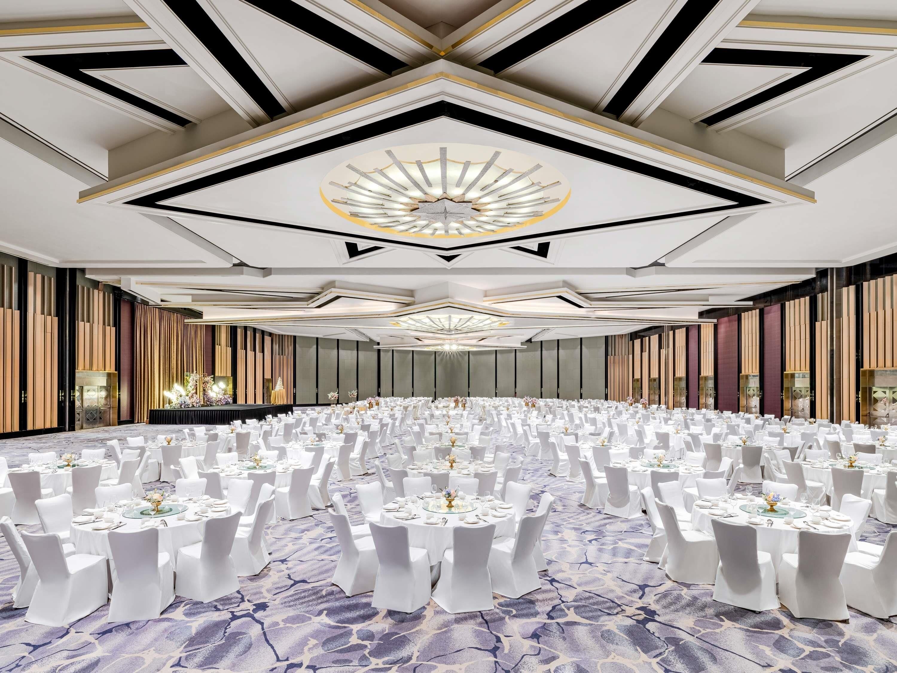 Un amplio salón de banquetes con mesas redondas dispuestas para un evento formal, con un diseño de techo moderno y una alfombra estampada.