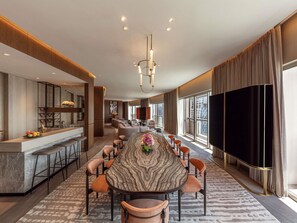 A modern dining area with a marble table, leather chairs, and a large TV screen.