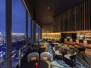 A high-rise bar with a city view, modern furniture, and a bar area with a well-stocked liquor display. - Fairmont Singapore (Singapore)