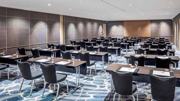 A conference room with rows of tables and chairs, a patterned carpet, and recessed ceiling lighting.