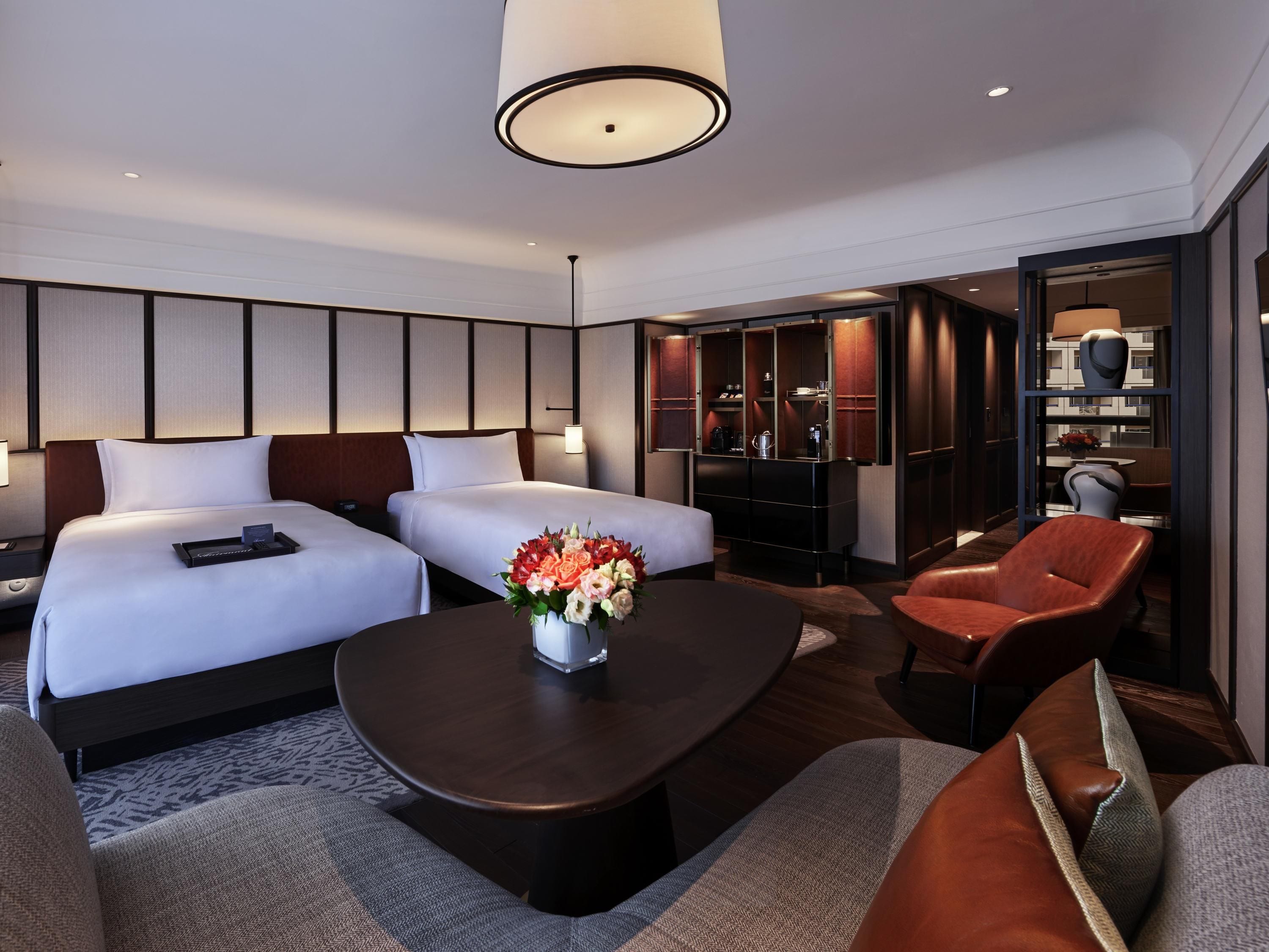 A hotel room with two beds, a coffee table, a sofa, a chair, and a minibar.