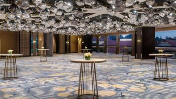 Un hall d’hôtel spacieux, doté d’un sol à motifs, de plusieurs tables rondes et d’un plafond orné de décorations sphériques réfléchissantes.