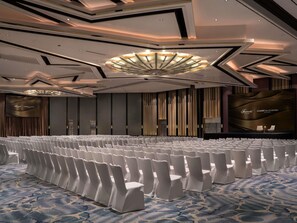 A conference room with rows of white chairs, a large screen, and a modern ceiling design.