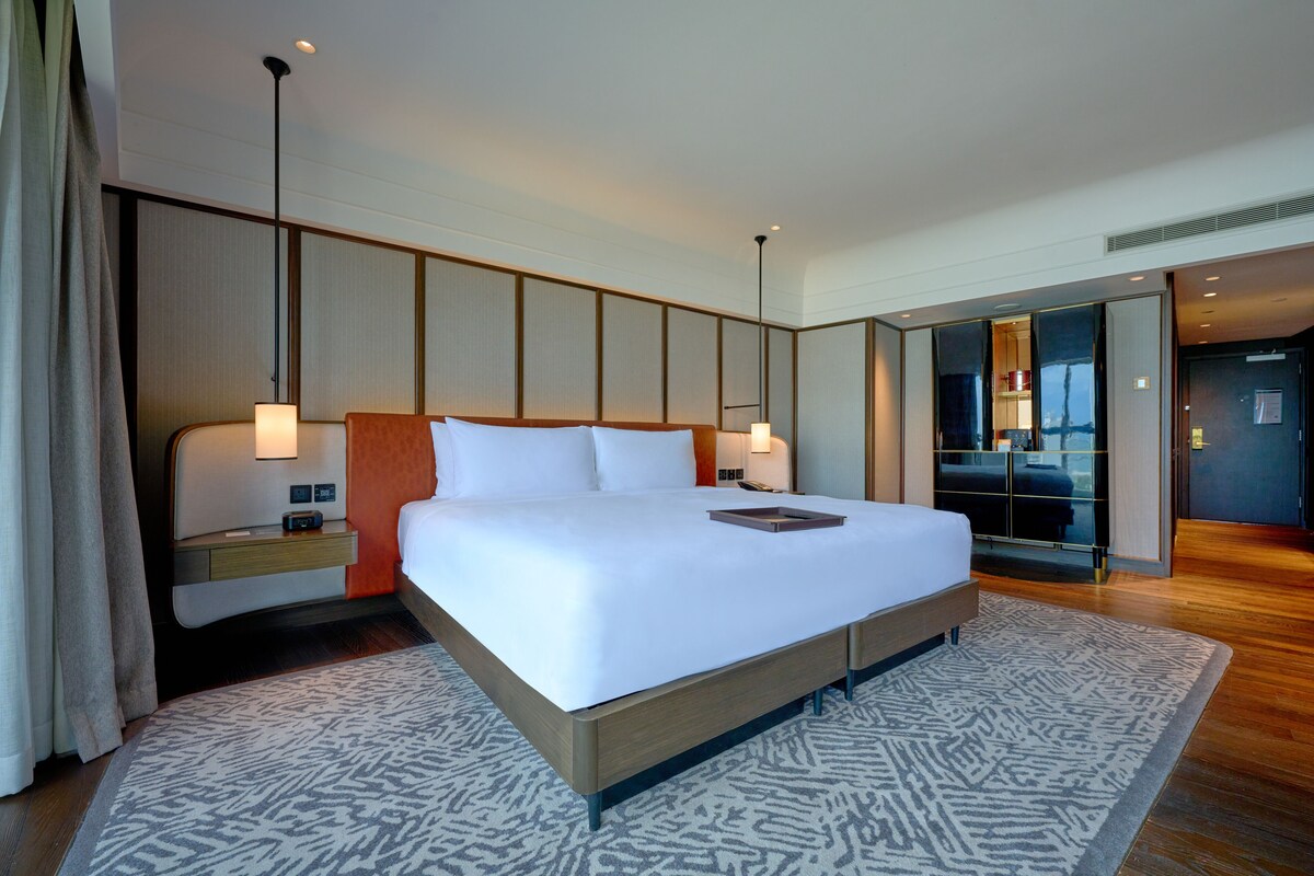 Een moderne hotelkamer met een groot bed, nachtkastjes en uitzicht op de stad door een glazen deur.