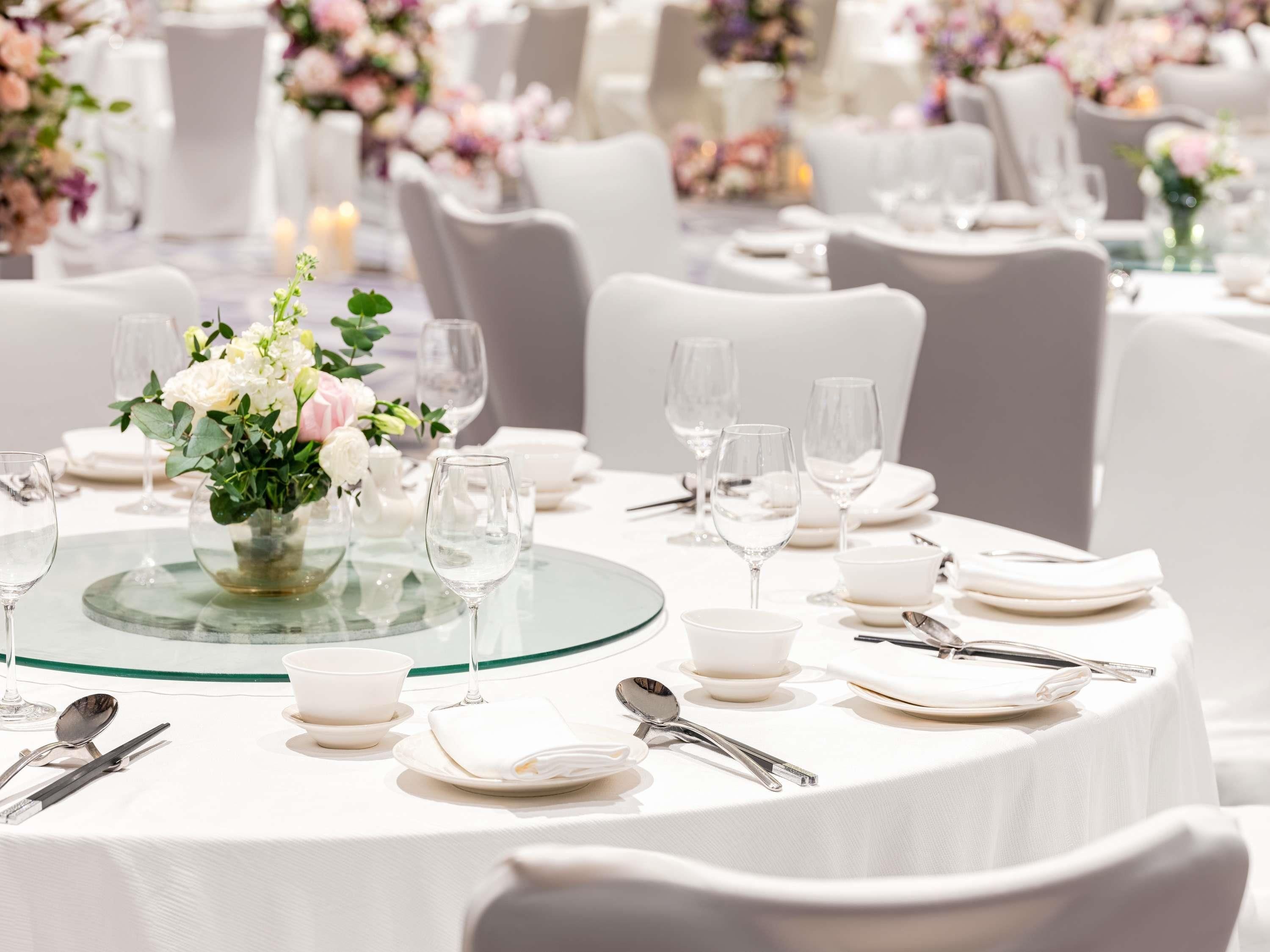 Una mesa dispuesta para un evento formal, con manteles blancos, cristalería y un centro de mesa floral.