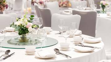 Una mesa dispuesta para un evento formal, con manteles blancos, cristalería y un centro de mesa floral.