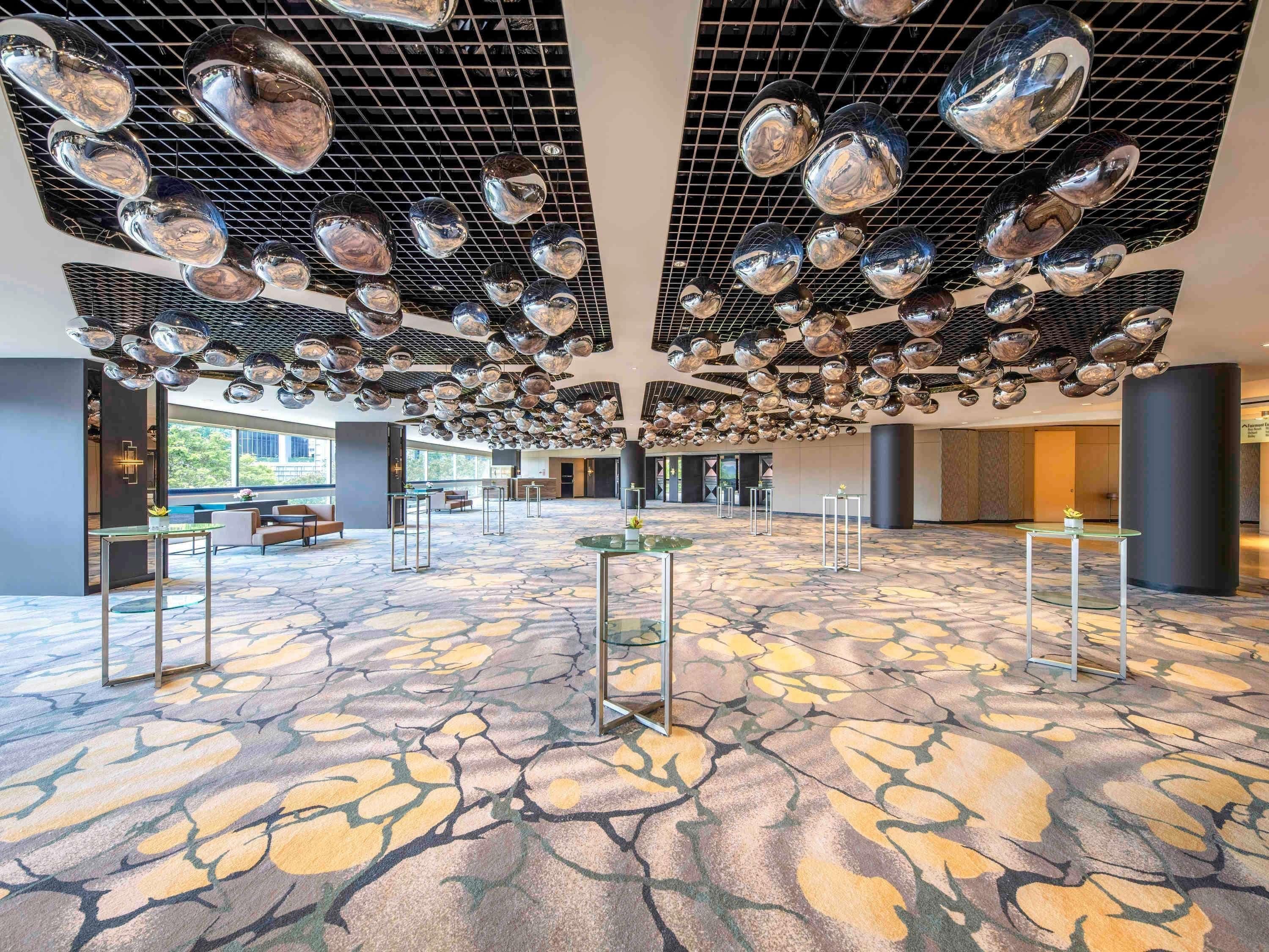 A spacious lobby with a patterned floor, multiple seating areas, and a ceiling adorned with reflective spherical decorations.
