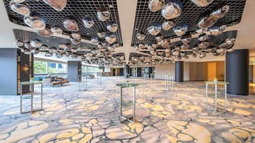 A spacious lobby with a patterned floor, multiple seating areas, and a ceiling adorned with reflective spherical decorations.