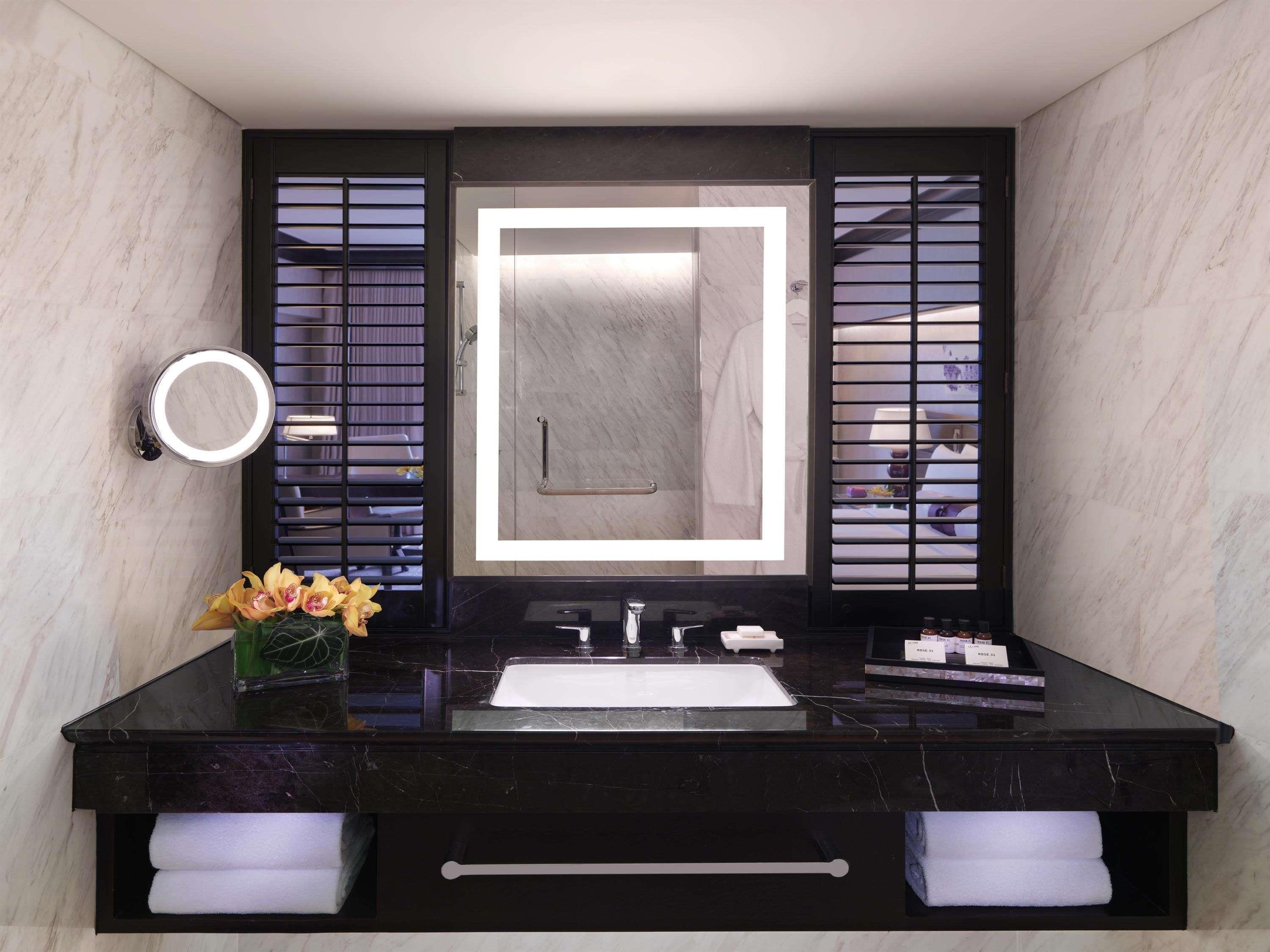 A modern bathroom with a black marble vanity, a large mirror with integrated lighting, and a vase with flowers.