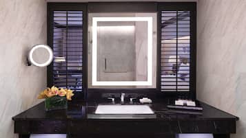 A modern bathroom with a black marble vanity, a large mirror with integrated lighting, and a vase with flowers.