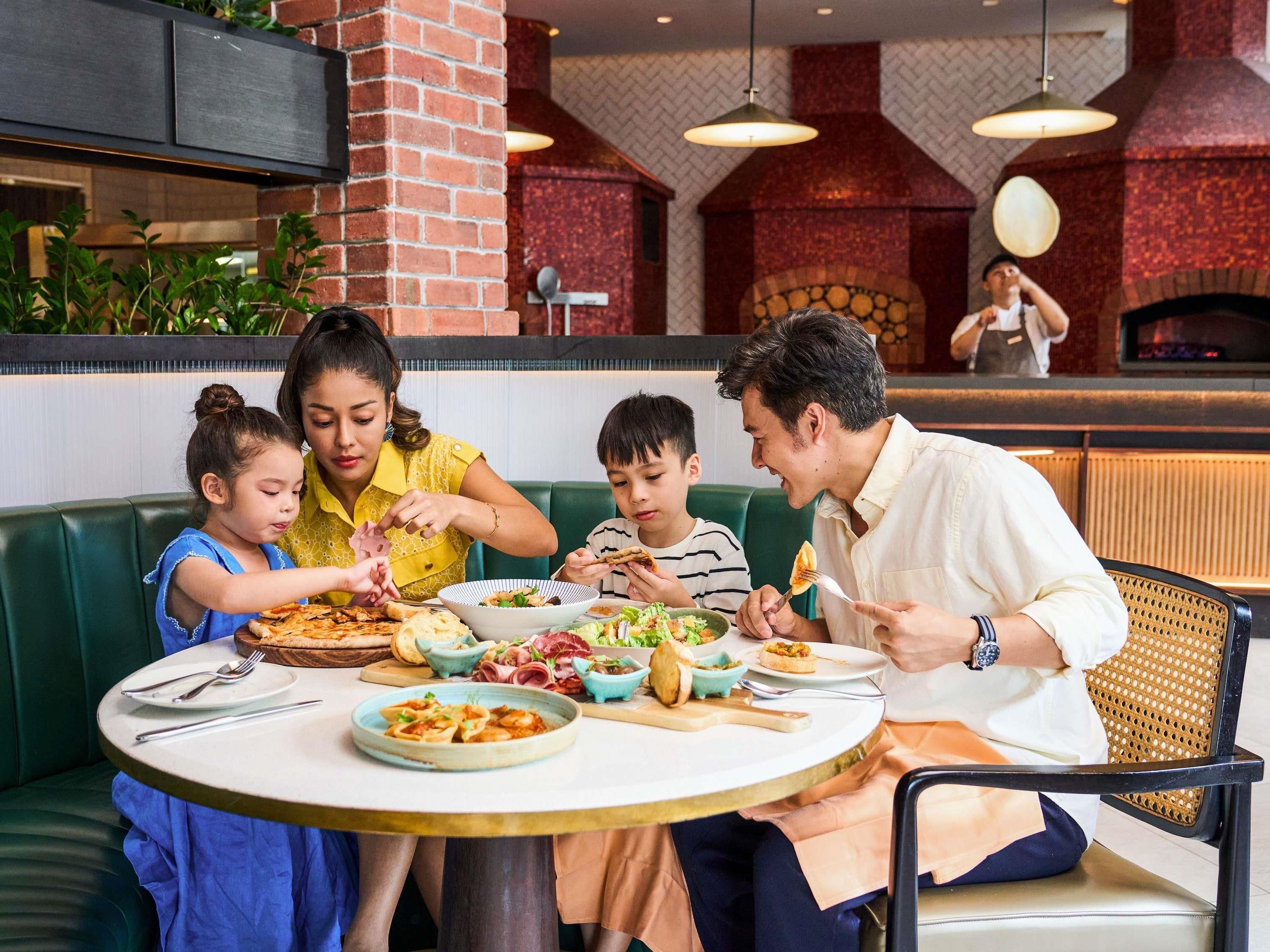 A family dining at a restaurant with a brick wall and a wood-fired oven in the background.