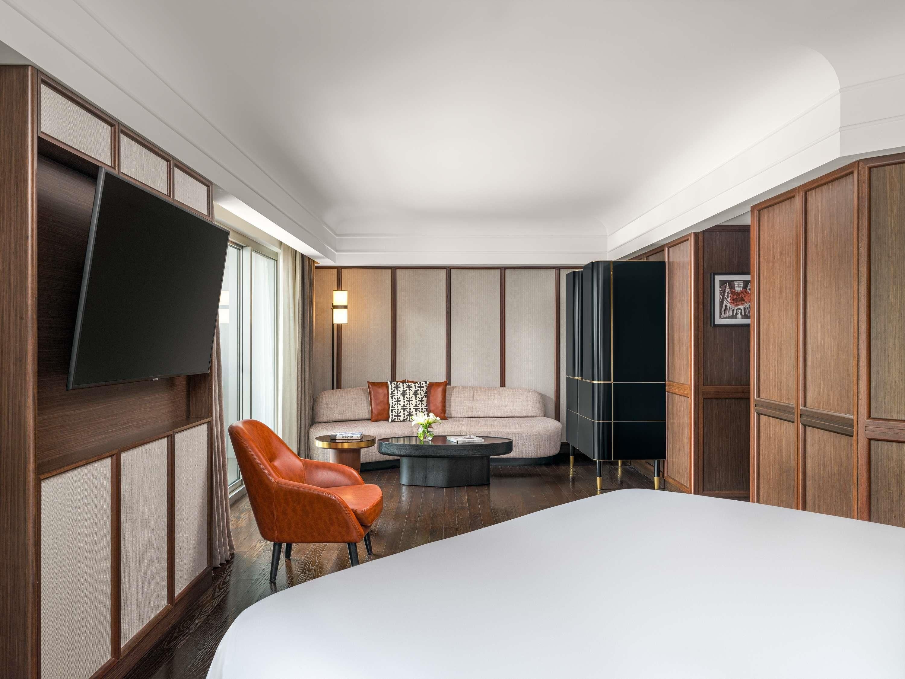 A hotel room with a large bed, a sofa, a chair, a coffee table, a flat-screen TV, and wooden paneling.