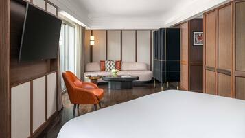 A hotel room with a large bed, a sofa, a chair, a coffee table, a flat-screen TV, and wooden paneling.